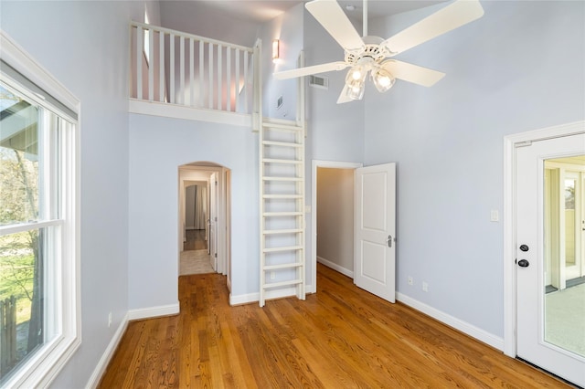 unfurnished bedroom with arched walkways, light wood-style flooring, multiple windows, and a towering ceiling