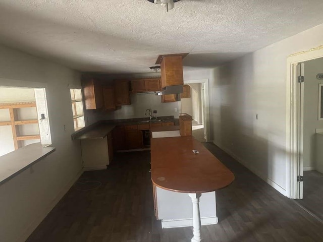 kitchen featuring dark wood-style floors, brown cabinets, dark countertops, a sink, and a textured ceiling