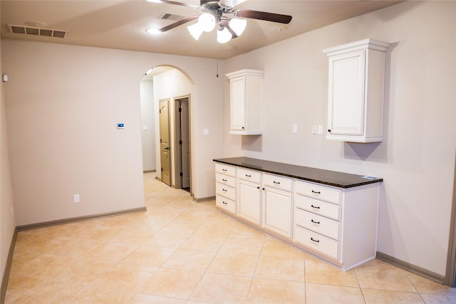 kitchen with visible vents, arched walkways, dark countertops, ceiling fan, and white cabinetry