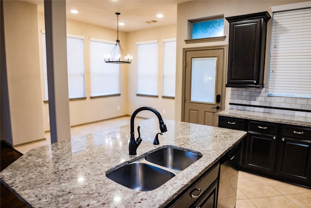 kitchen with decorative backsplash, dishwashing machine, light stone countertops, pendant lighting, and a sink