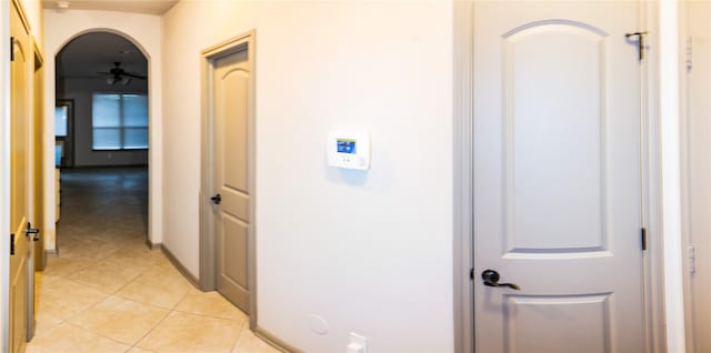 corridor featuring light tile patterned floors, baseboards, and arched walkways