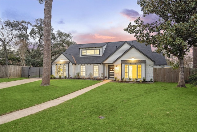 view of front facade featuring a yard, concrete driveway, brick siding, and fence