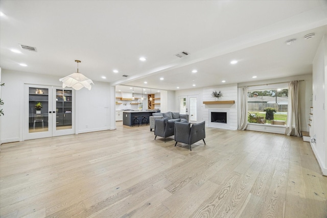 living area featuring light wood-type flooring, french doors, visible vents, and a fireplace