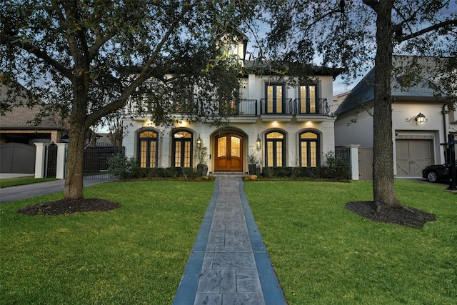 view of front facade featuring a balcony, fence, french doors, a front lawn, and stucco siding