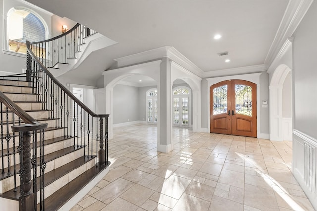 foyer entrance with visible vents, arched walkways, ornamental molding, and french doors