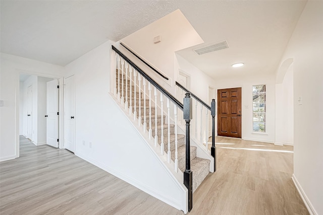 stairs featuring arched walkways, visible vents, baseboards, and wood finished floors