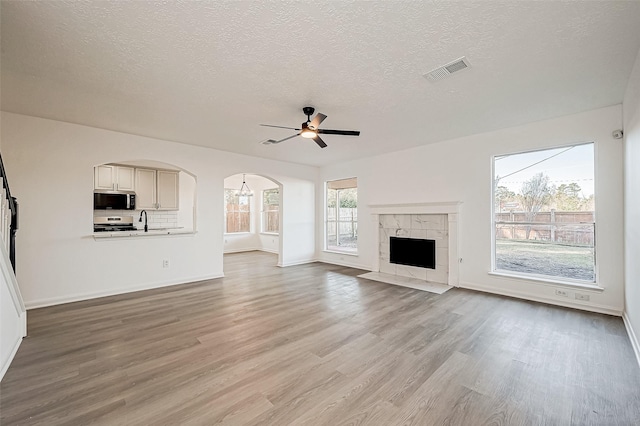 unfurnished living room with arched walkways, visible vents, light wood-style flooring, ceiling fan, and a sink