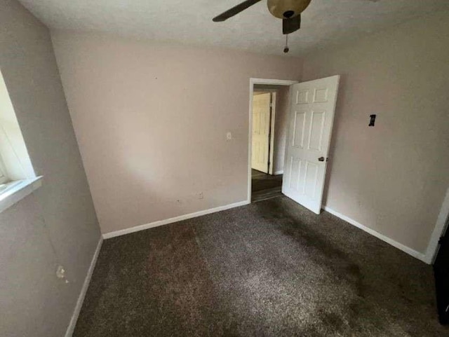 unfurnished bedroom with dark colored carpet, a ceiling fan, and baseboards