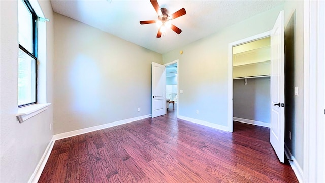 unfurnished bedroom with ceiling fan, a spacious closet, wood finished floors, and baseboards