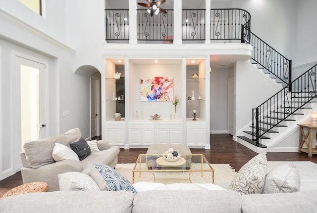 living area featuring arched walkways, a high ceiling, dark wood-style flooring, and baseboards