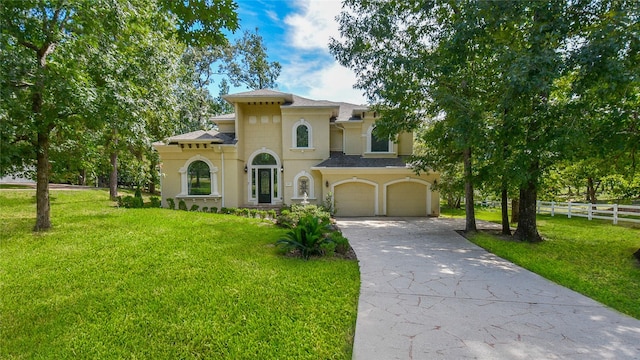 mediterranean / spanish-style house featuring driveway, an attached garage, fence, a front yard, and stucco siding