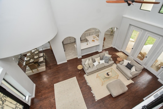 living area featuring baseboards, a high ceiling, arched walkways, and dark wood-style flooring