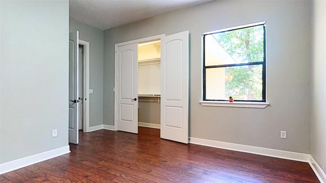 unfurnished bedroom with a closet, dark wood finished floors, a textured ceiling, and baseboards