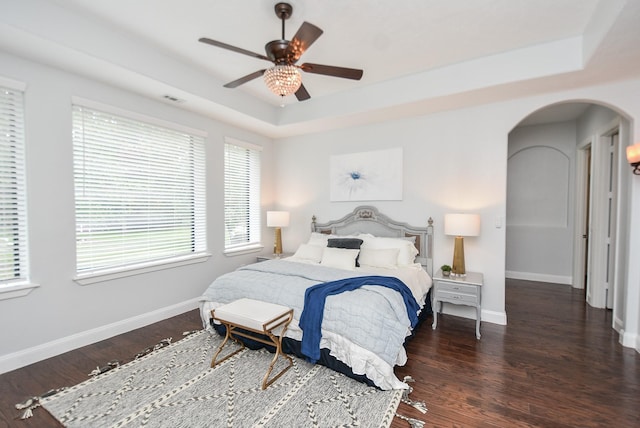 bedroom featuring dark wood-style floors, baseboards, arched walkways, and a raised ceiling