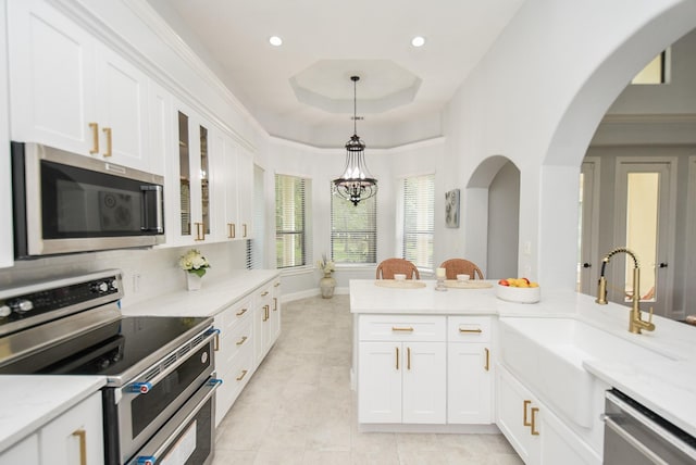 kitchen with light stone counters, appliances with stainless steel finishes, glass insert cabinets, and white cabinetry