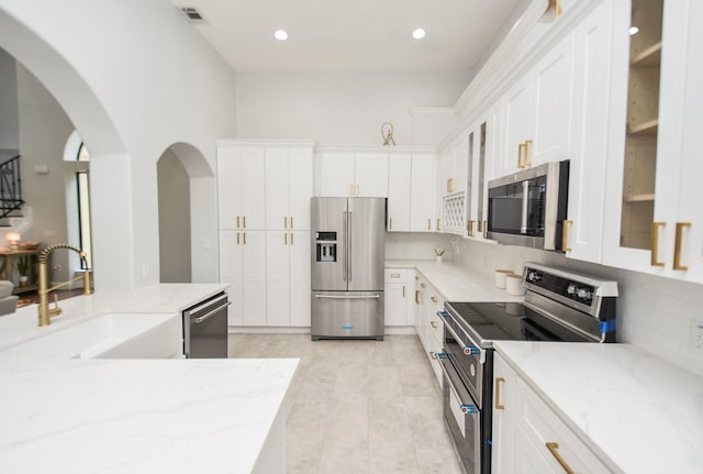 kitchen with light stone counters, stainless steel appliances, visible vents, glass insert cabinets, and white cabinetry