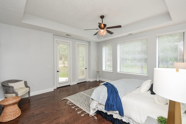 bedroom featuring dark wood-type flooring, access to outside, a raised ceiling, and baseboards