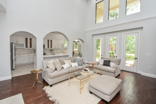 living room featuring dark wood-type flooring, arched walkways, a towering ceiling, and baseboards