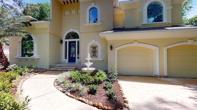 doorway to property with a garage, a shingled roof, concrete driveway, and stucco siding