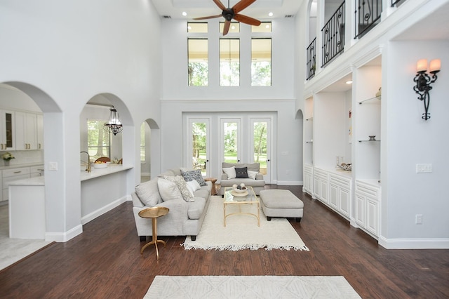 living area featuring arched walkways, ceiling fan, dark wood-style flooring, and baseboards