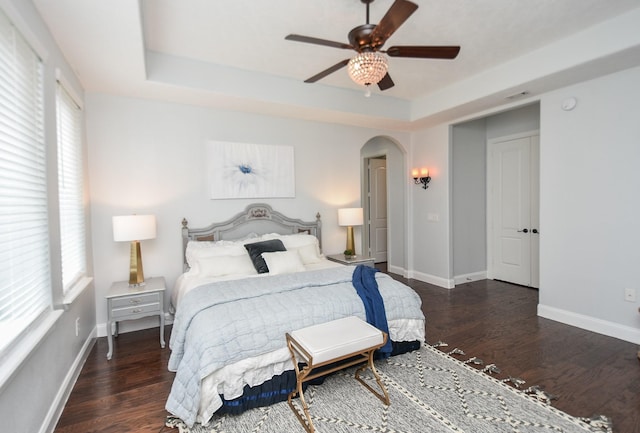 bedroom featuring baseboards, a tray ceiling, arched walkways, and dark wood finished floors