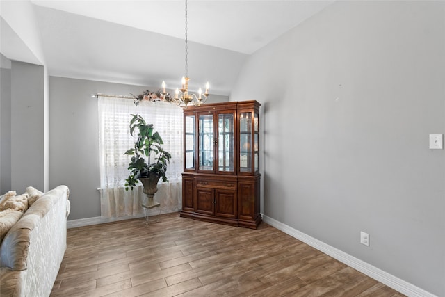 dining space with a chandelier, vaulted ceiling, baseboards, and wood finished floors