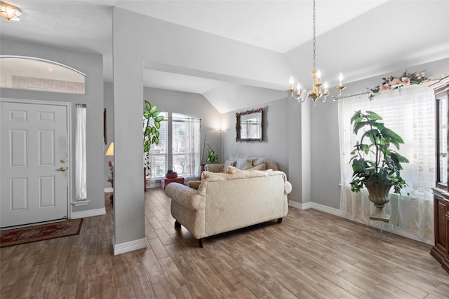 living area with baseboards, a chandelier, vaulted ceiling, and wood finished floors