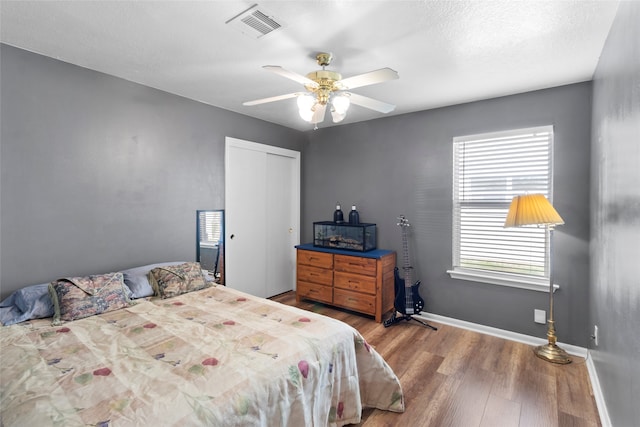 bedroom featuring ceiling fan, wood finished floors, visible vents, baseboards, and a closet