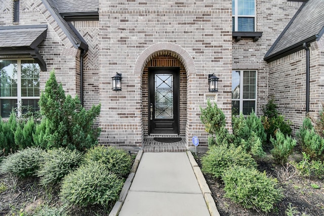 view of exterior entry featuring roof with shingles and brick siding