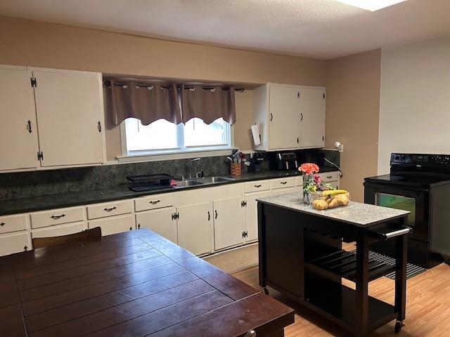 kitchen with dark countertops, light wood-style flooring, white cabinets, a sink, and black range with electric cooktop