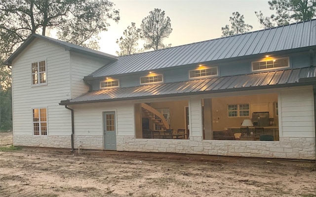 back of property at dusk featuring stone siding and metal roof