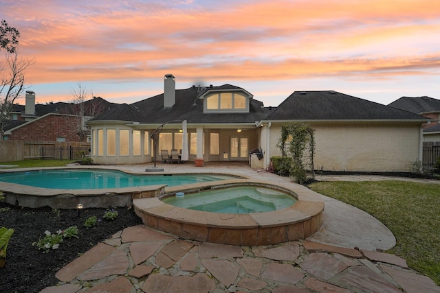 back of property at dusk featuring a fenced in pool, a chimney, an in ground hot tub, fence, and a patio area