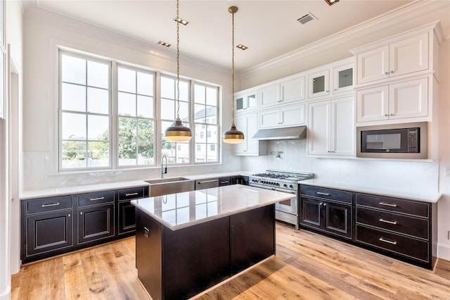 kitchen featuring under cabinet range hood, a kitchen island, white cabinetry, appliances with stainless steel finishes, and glass insert cabinets