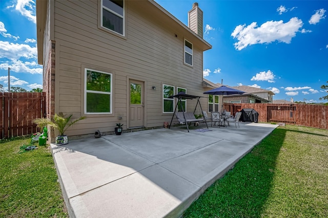 back of house featuring a fenced backyard, a patio, a chimney, and a lawn