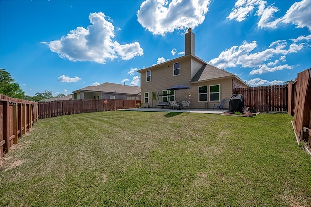 rear view of property with a fenced backyard, a yard, a chimney, and a patio