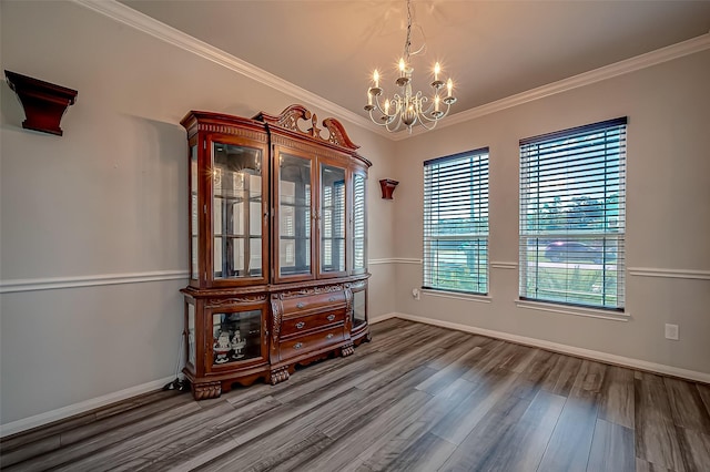 unfurnished dining area featuring an inviting chandelier, crown molding, baseboards, and wood finished floors