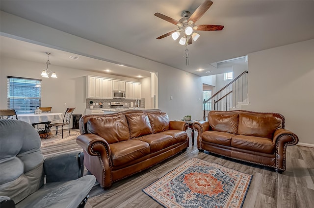 living room with stairs, wood finished floors, and ceiling fan with notable chandelier