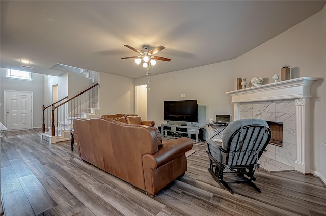 living room with a fireplace, visible vents, stairway, ceiling fan, and wood finished floors