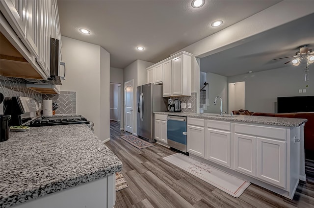 kitchen featuring stainless steel appliances, a peninsula, a sink, and white cabinetry