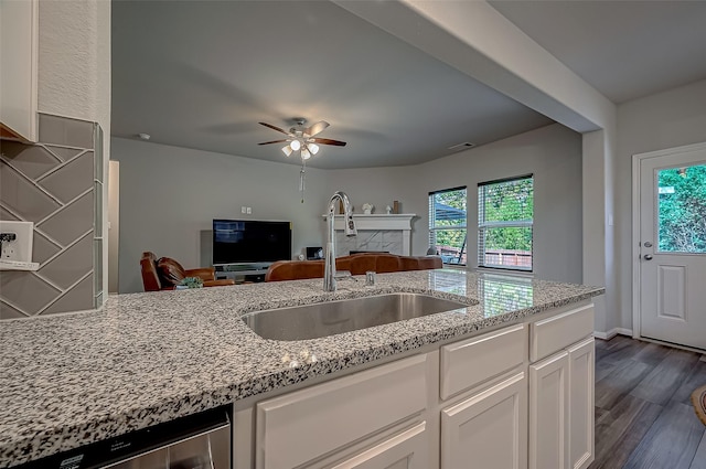 kitchen featuring light stone counters, open floor plan, white cabinets, and a sink