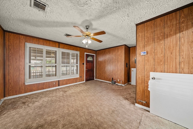 carpeted empty room with wooden walls, visible vents, and a ceiling fan