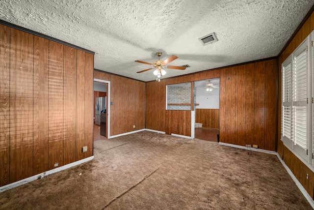 carpeted empty room featuring visible vents, a ceiling fan, crown molding, a textured ceiling, and wood walls