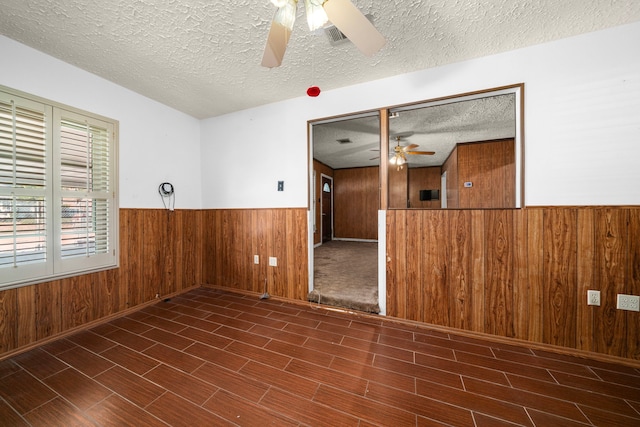 unfurnished room with a ceiling fan, wainscoting, a textured ceiling, wood finish floors, and wood walls