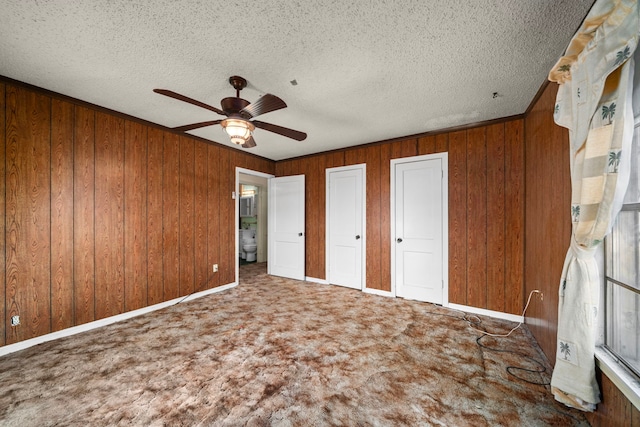 unfurnished bedroom featuring multiple closets, carpet flooring, a textured ceiling, and wooden walls