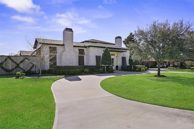 view of front of home featuring stone siding, concrete driveway, a chimney, and a front lawn