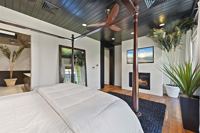 bedroom with a warm lit fireplace, wood ceiling, wood finished floors, and visible vents