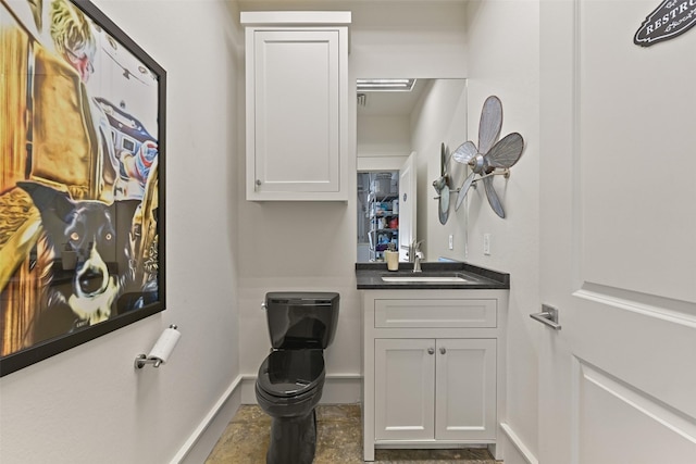 half bathroom featuring toilet, baseboards, and vanity