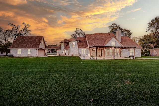 back of house at dusk with a patio area, a chimney, stone siding, and a lawn