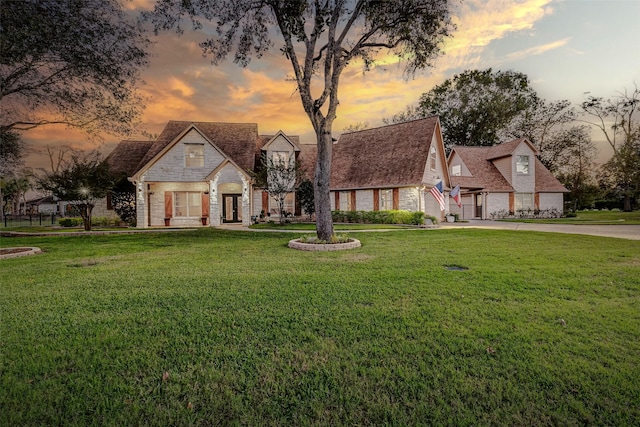 view of front facade featuring driveway, stone siding, a garage, and a lawn