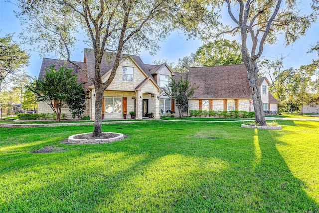 french country home featuring stone siding, roof with shingles, and a front lawn